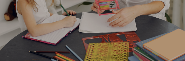 A tutor and student working together at a table, using paper, stencils, pencils, and coloured pencils.