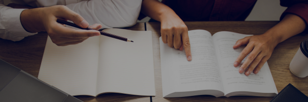 A person with a pencil pointing at a book while another person reads along.