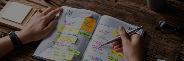A person is reviewing their daily schedule, which is filled with colorful sticky notes and handwritten tasks.