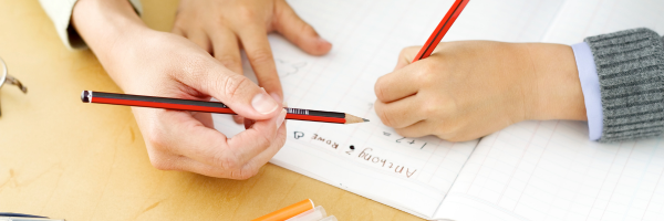 A child and adult writing together at a desk.