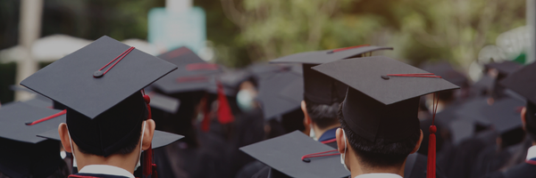 A group of graduates in caps and gowns, seen from behind, with their black mortarboards and red tassels, creating a scene of a graduation ceremony.