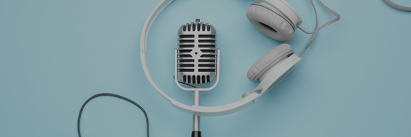 A retro silver microphone with a white headset wrapped around it sits on a light blue background.