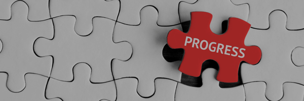 That's an impactful image! It features a jigsaw puzzle with one piece, colored bright red and labeled "PROGRESS" in white text, sitting slightly out of place next to the hole it should fit into. The rest of the puzzle pieces are a uniform, muted white/grey.