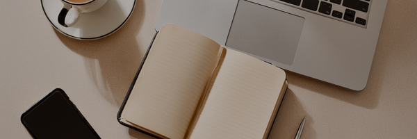 A top-down view of a workspace featuring an open notebook, a laptop, a smartphone, and a cup of coffee on a beige desk.